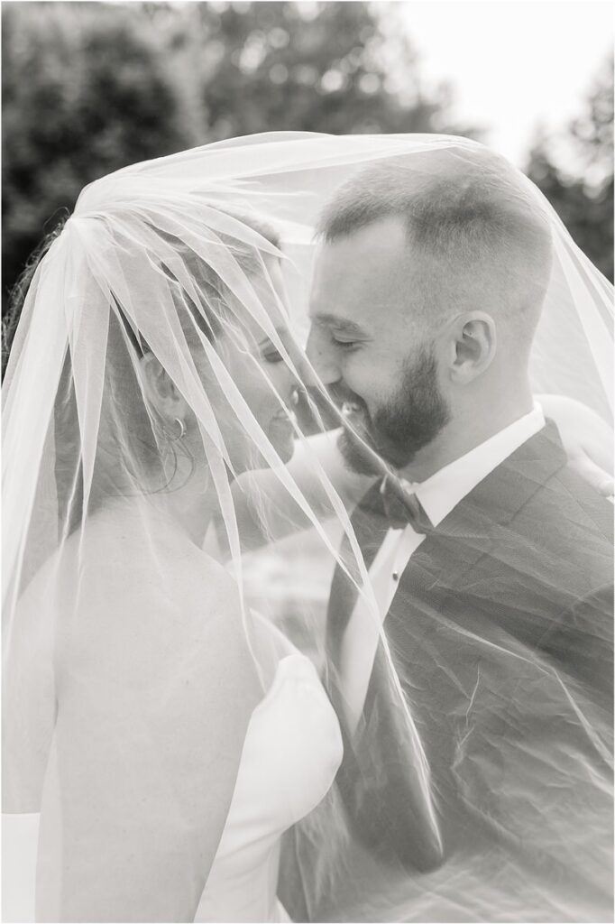 Husband and wife smile together under veil for Summer Maine Wedding