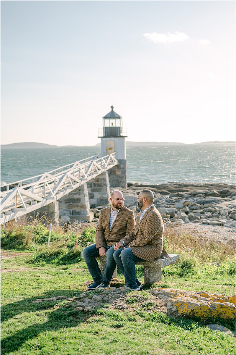 Two men sit on rocks and smile at one another before their Maine fall elopement